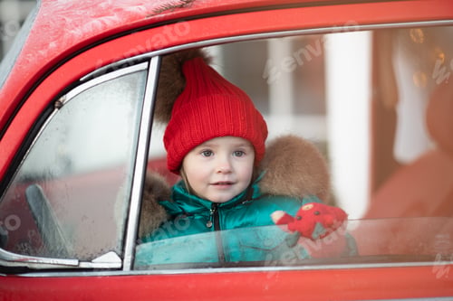 Preview: Smiling cute winter girl in red hat sitting in car having fun