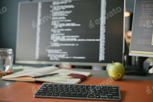 Preview: Closeup of Wireless Keyboard on Desk with Computer Screen Displaying Code