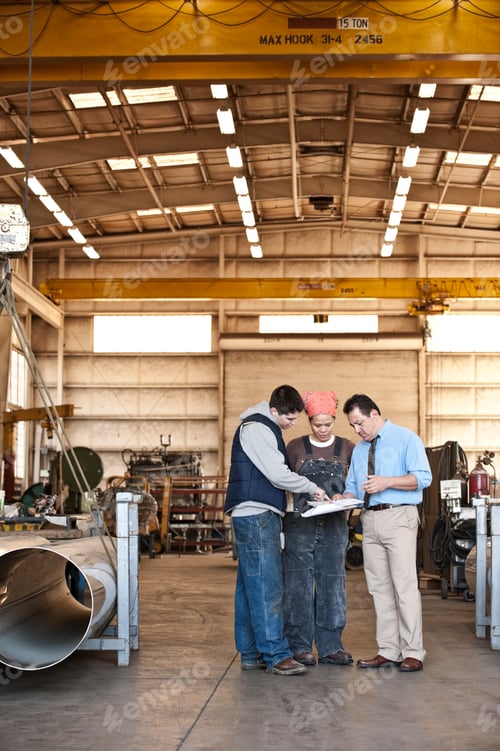 Preview: Mixed race team of workers and management people in a large sheet metal factory
