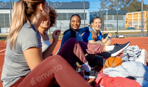 Preview: Diverse group of young woman sitting on court resting afrer playing basketball outdoors.