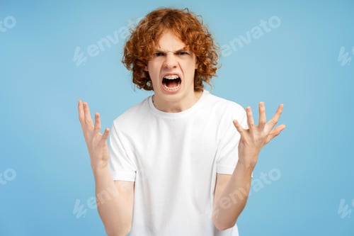 Preview: Angry boy wearing white t shirt screaming looking at camera isolated on blue background