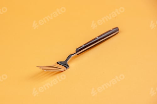 Preview: Side view of shiny stainless metal fork lying on peach wave background with free space
