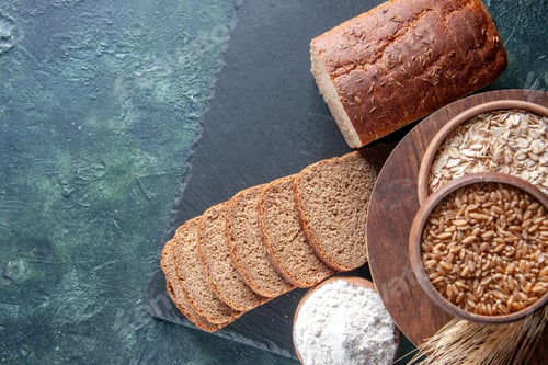 Preview: Above view of black bread slices on black tray and flour in brown bowl on the left side on dark