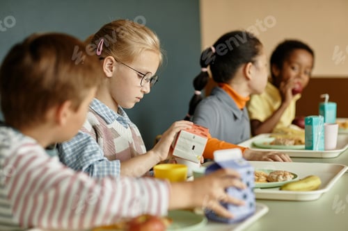 Preview: Girl Pouring Drink in Cup Sitting at Table while Eating Lunch in School Cafeteria