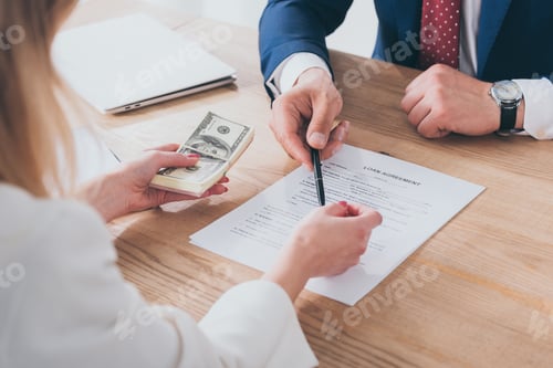 Preview: cropped shot of businessman pointing at signature place in loan agreement near woman holding dollar