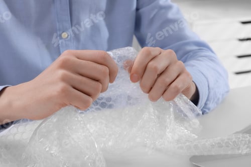 Preview: Woman popping bubble wrap at table in office, closeup. Stress relief