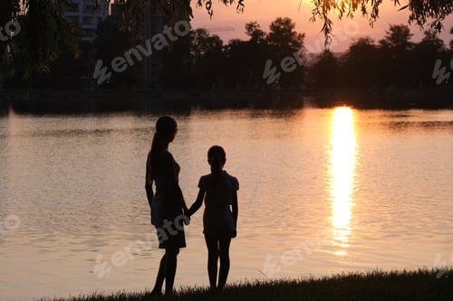 Preview: Happy mother and daughter standing together holding hands enjoying time in summer park in evening
