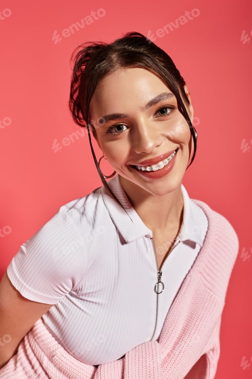 Preview: Joyful young woman smiling brightly in a vibrant studio setting with pink background