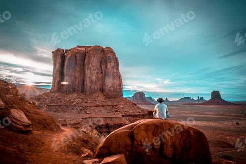 Preview: A boy in a white T-shirt sitting on a stone in the sunset inside Monument Valley