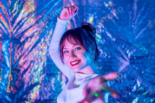Preview: Happy smiling woman in white clothes dancing in neon light and extends a hand inviting you. White