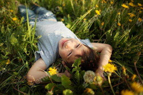 Preview: Smiling little boy lie in green grass and dandelions in summertime