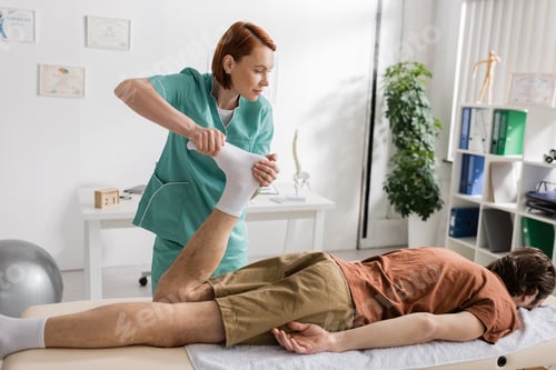 Preview: osteopath massaging painful feet of man lying on massage table in consulting room