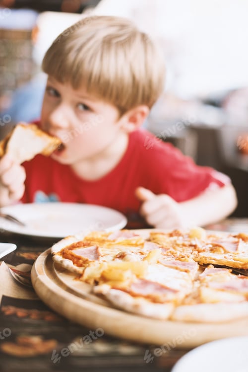 Preview: Boy bringing pizza slice up to his mouth to eat. Kids being kids Defocused face. Background