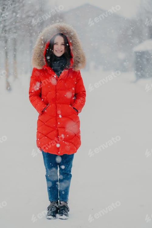 Preview: Full length vertical shot of pretty woman wears red winter jacket, jeans and boots