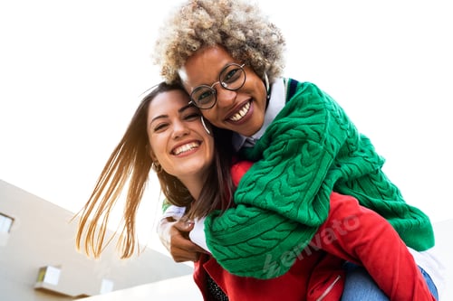 Preview: Playful multiracial lesbian couple looking at camera. Woman piggyback ride girlfriend. Copy space.