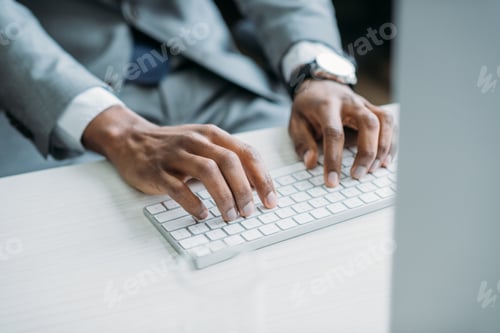 Preview: partial view of african american businessman typing on keyboard at workplace