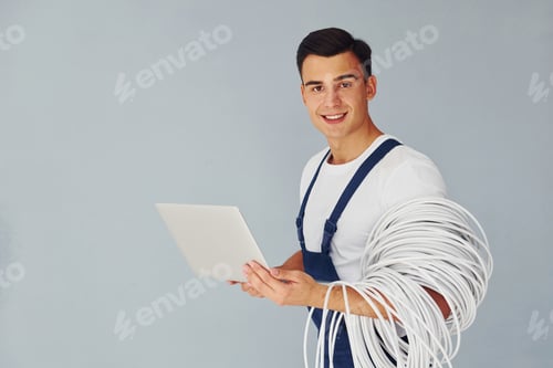 Preview: Uses laptop. Male worker in blue uniform standing inside of studio against white background