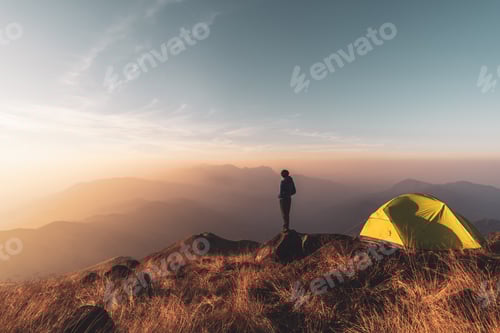 Preview: Young man traveler looking landscape at sunset and camping on mountain