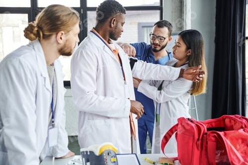 Preview: healthcare worker helping asian student applying compressive tourniquet on arm of african american