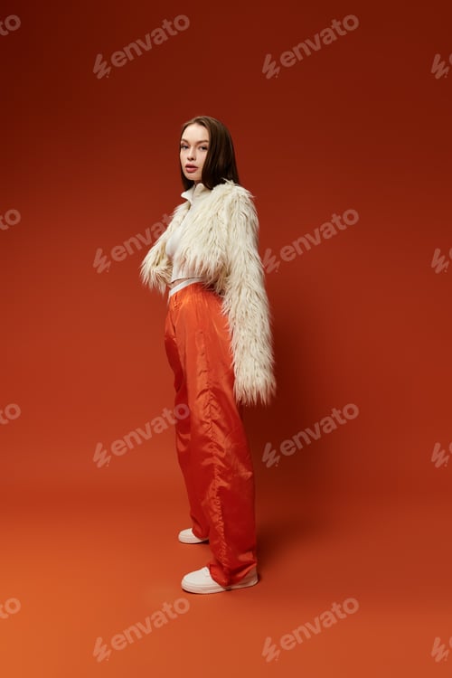 Preview: Vibrant stylish woman posing confidently in a striking orange setting during a fashion showcase