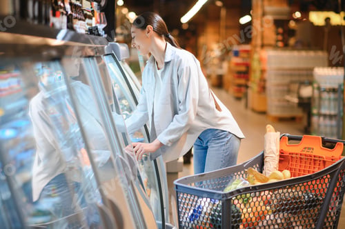 Preview: Happy young woman looking at product at grocery store. Smiling woman shopping in supermarket