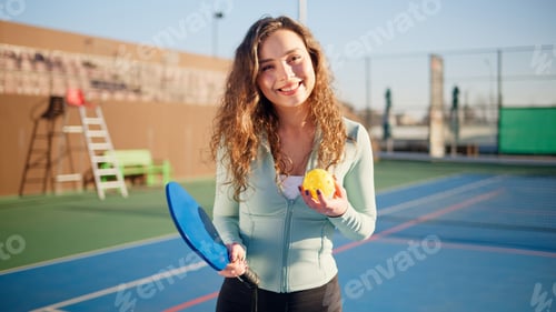 Preview: Portait of a young, happy and smiling curly haired girl holding pickleball paddle