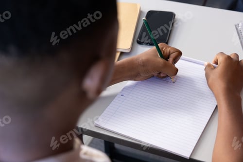 Preview: Writing in notebook, student focusing on schoolwork at desk with smartphone nearby