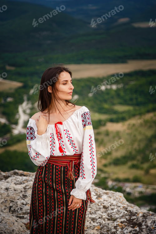 Preview: Attractive woman in traditional romanian costume on mountain green blurred background.