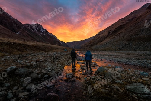 Preview: Lovely view of people standing on rocks in a shallow lake in the mountains, looking at the sunset