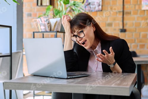 Preview: Cheerful talking middle-aged woman having video call using laptop in coworking cafe