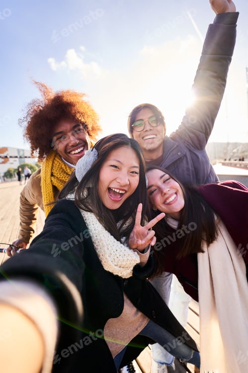 Preview: Cheerful group of friends taking a selfie outdoors in the city, smiling and looking at camera.