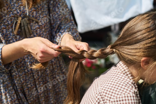 Preview: Woman Braiding Hair of Young Girl Outdoors