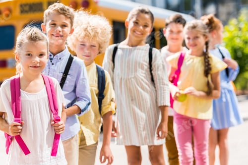 Preview: group of adorable schoolchildren standing in row in front of school bus and looking at camera