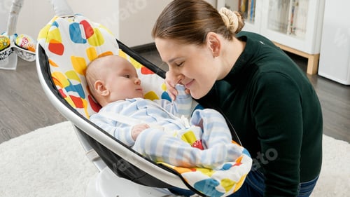 Preview: Happy smiling mother playing with her little baby son sitting in electric rocking chair at home