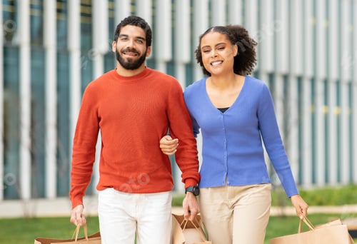 Preview: Happy Multicultural Buyers Couple Holding Paper Shopping Bags Walking Outdoors