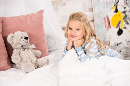 Preview: adorable kid with teddy bear in bed looking at camera