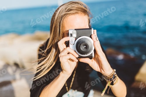 Preview: Young woman taking picture with old-fashioned camera at the seafront