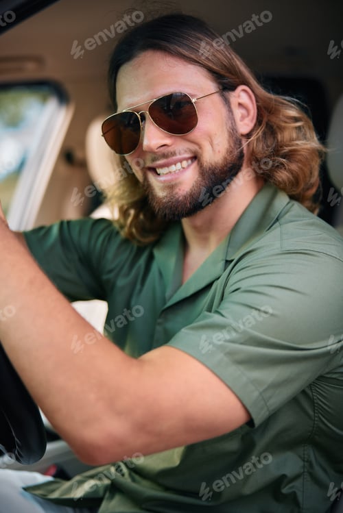 Preview: Smiling man with sunglasses in a car, wearing a green shirt, conveying a sense of freedom and