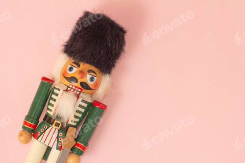 Preview: Interesting beautiful christmas nutcracker soldier on pink colored paper surface texture with copy s