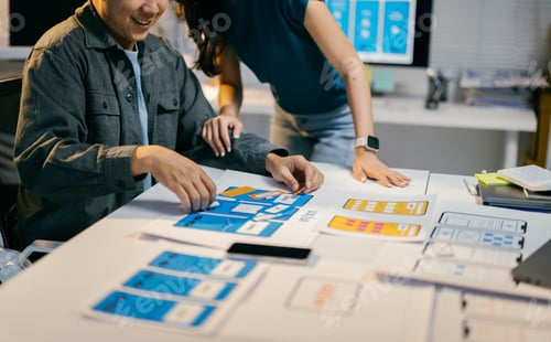 Preview: Two designers collaborate on a mobile app wireframe, discussing ideas for a user-friendly interface.