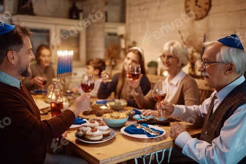 Preview: Happy multi-generation Jewish family toasting during a meal at dining table on Hanukkah.