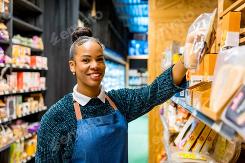 Preview: Smiling saleswoman arranging products on shelves in organic supermarket