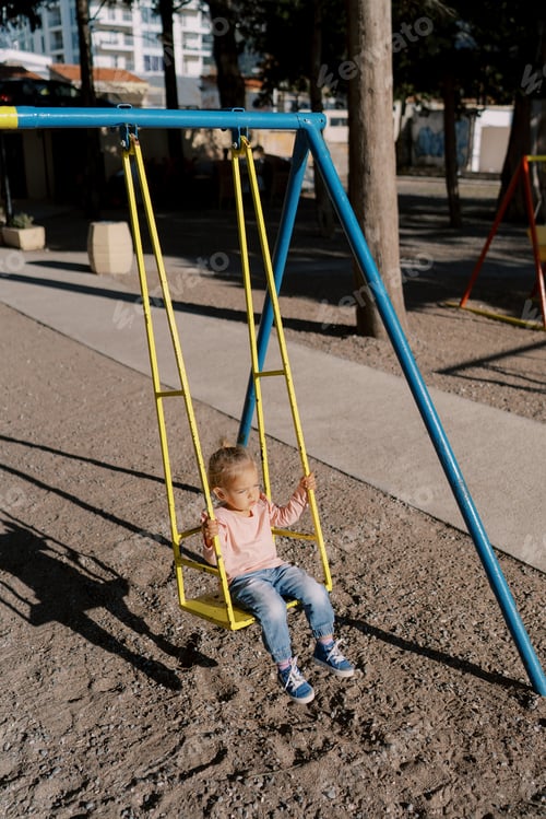 Preview: Little girl swinging on a swing under bright sunlight