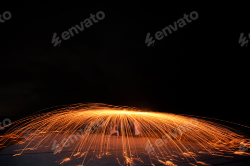 Preview: Closeup shot of a firestarter performing an amazing fire show with sparkles in the nighttime