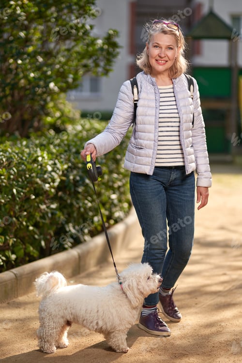 Preview: Adult Blond Woman Walking With Fluffy White Dog In City Park.