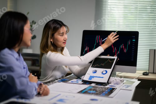 Preview: Businesswomen analyzing financial charts and graphs on computer and documents