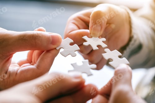 Preview: Closeup image of many people holding and putting a piece of white jigsaw puzzle together