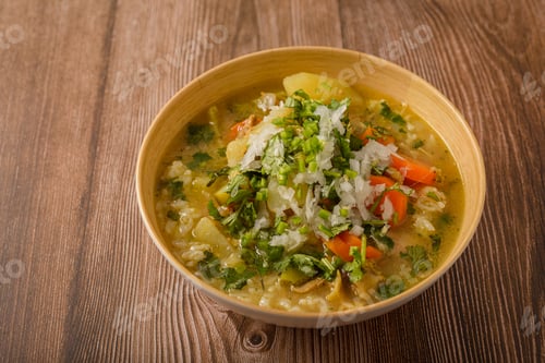 Preview: Chicken soup with vegetables in a deep bowl on a wooden table.