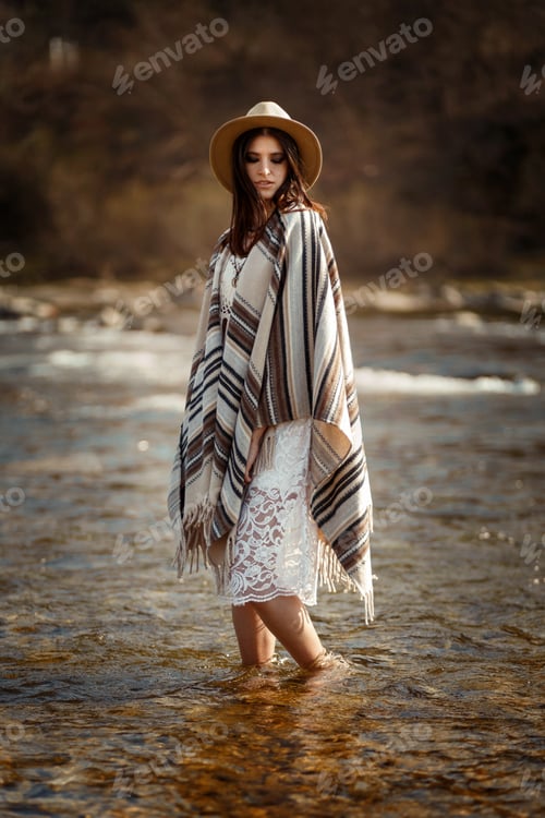Preview: beautiful woman traveler wearing hat and poncho standing in water of river