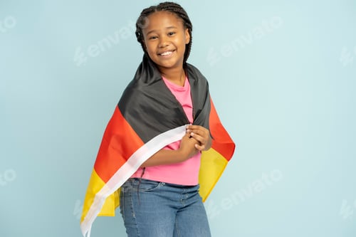 Preview: Positive Nigerian girl holding German flag wrapped in it isolated on blue background